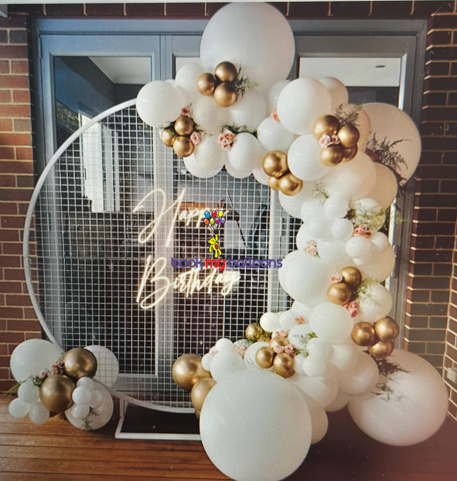 Gold and white balloon birthday backdrop with mesh stand and flowers